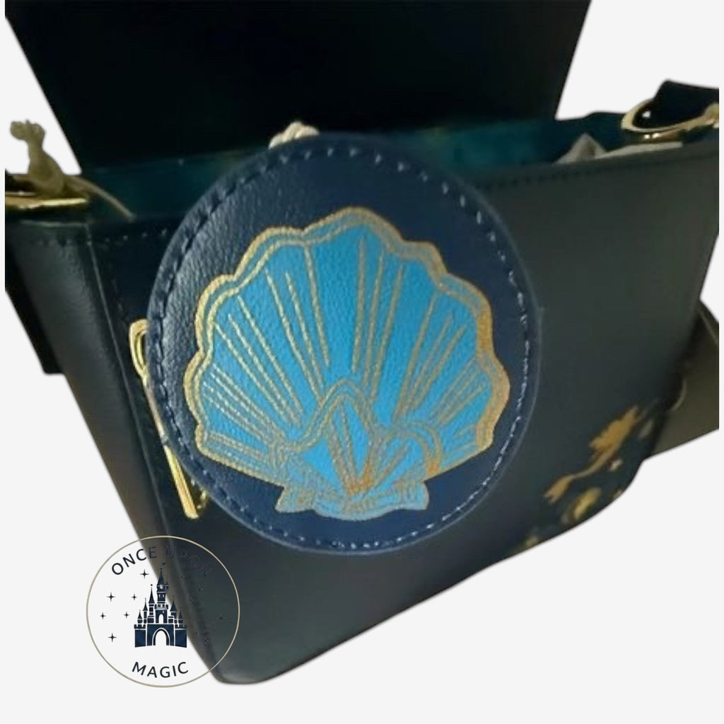 Once Upon Magic dark blue faux leather crossbody bag with a gold trimmed blue seashell applique and Ariel silhouette detail.