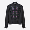 Once Upon Magic black long-sleeve blouse with embroidered floral details in purple, pink, and blue, featuring ruffled front and high neck.