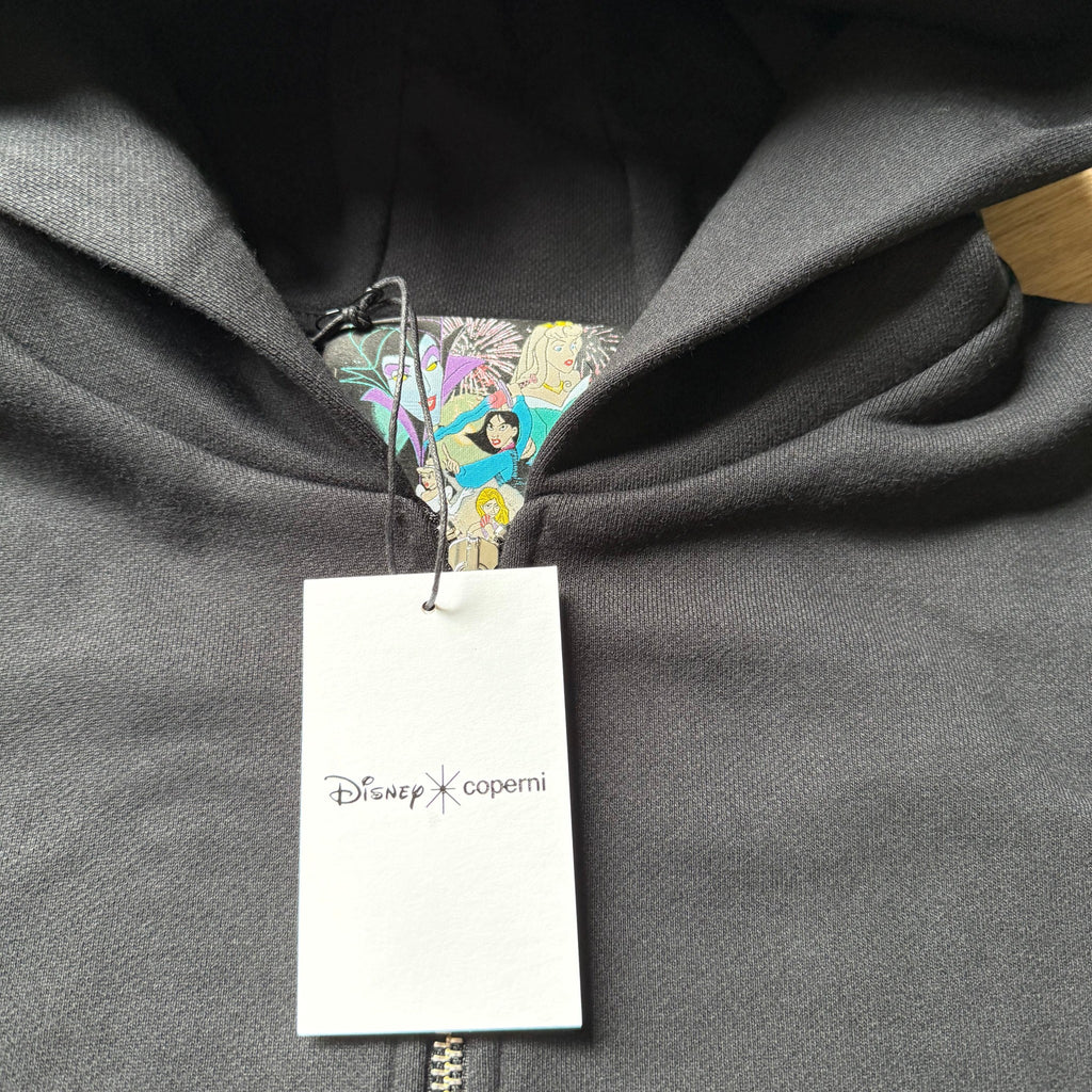 Once Upon Magic black zip-up hoodie featuring a Disney x Coperni tag and a colorful character print inside the hood.
