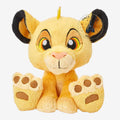 Once Upon Magic Disney Big Feet Simba plush toy, yellow with black-tipped ears and large paws, sitting against a sunset backdrop.