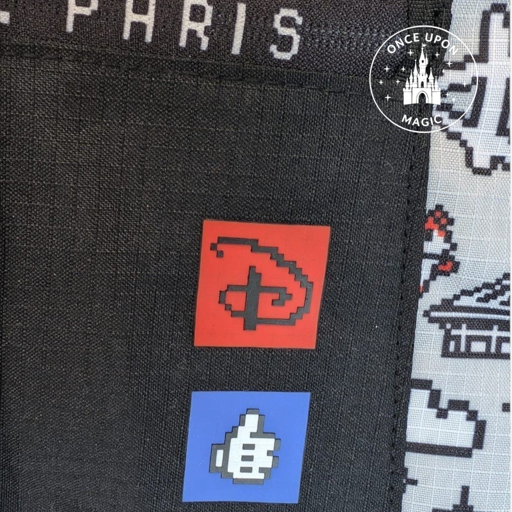 Sac à dos noir avec logo Disney pixelisé rouge et pouce levé pixelisé bleu, inscription Disneyland Paris. Par Once Upon Magic.