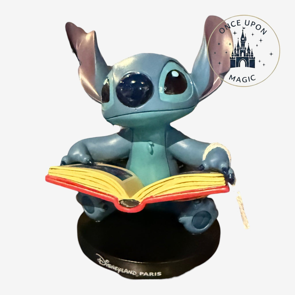 Once Upon Magic blue Stitch figurine sitting and reading an open book on a black Disneyland Paris base.