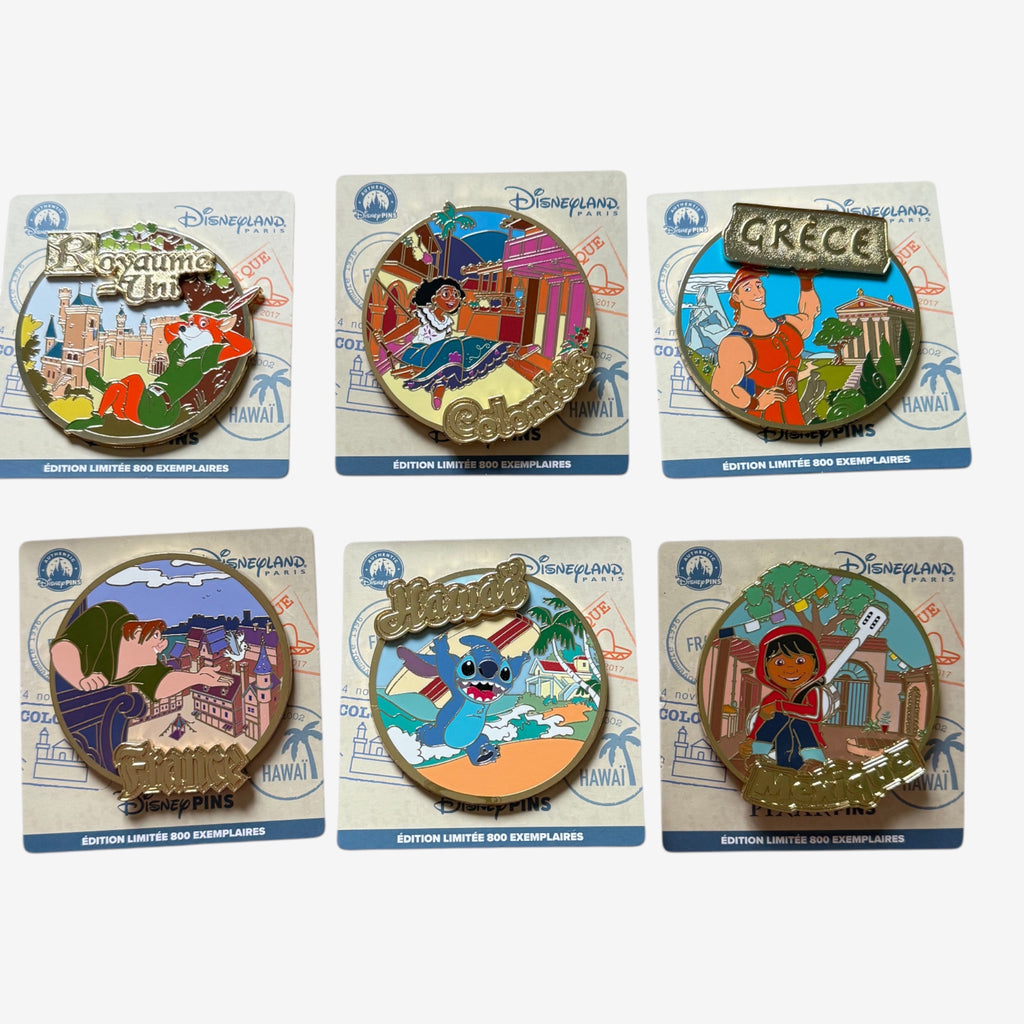 Once Upon Magic collection of six Disney character enamel pins featuring travel themes: Robin Hood in the UK, Mirabel in Colombia, Hercules in Greece, Quasimodo in France, Stitch in Hawaii, and Miguel from Coco.