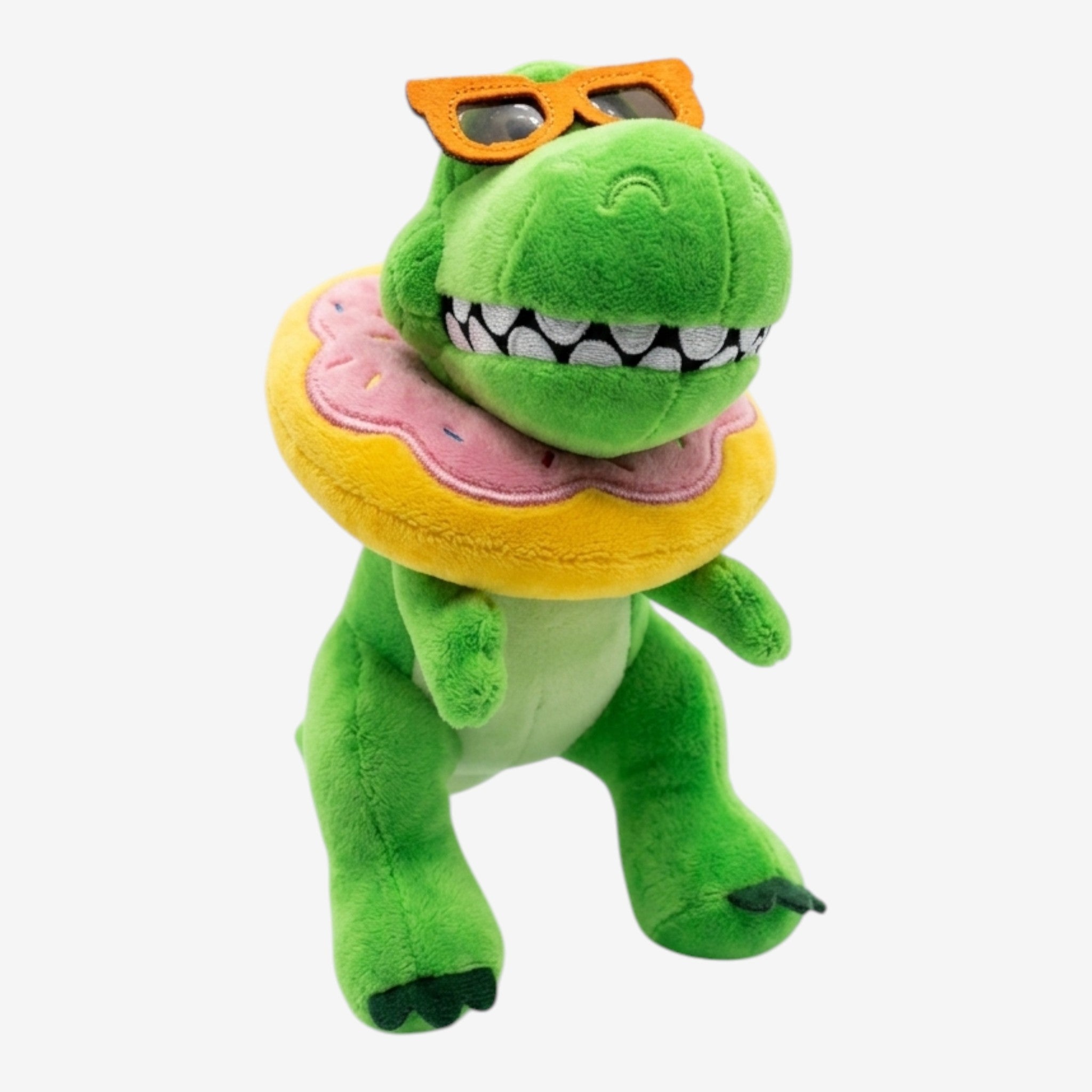 Peluche dinosaure vert Once Upon Magic avec lunettes de soleil orange et tour de cou beigne rose et jaune.