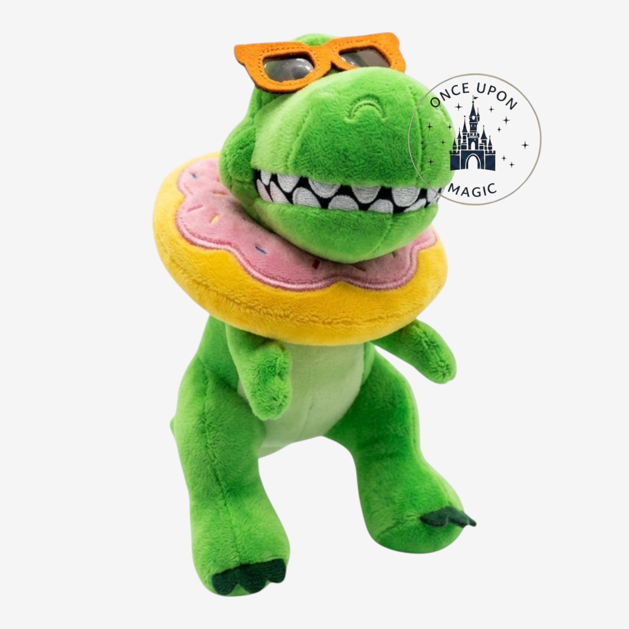 Peluche dinosaure vert Once Upon Magic avec lunettes de soleil orange et tour de cou beigne rose et jaune.