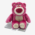 Peluche ours rose Lotso de Once Upon Magic, avec nez rouge et ventre beige, assis sur une carte.