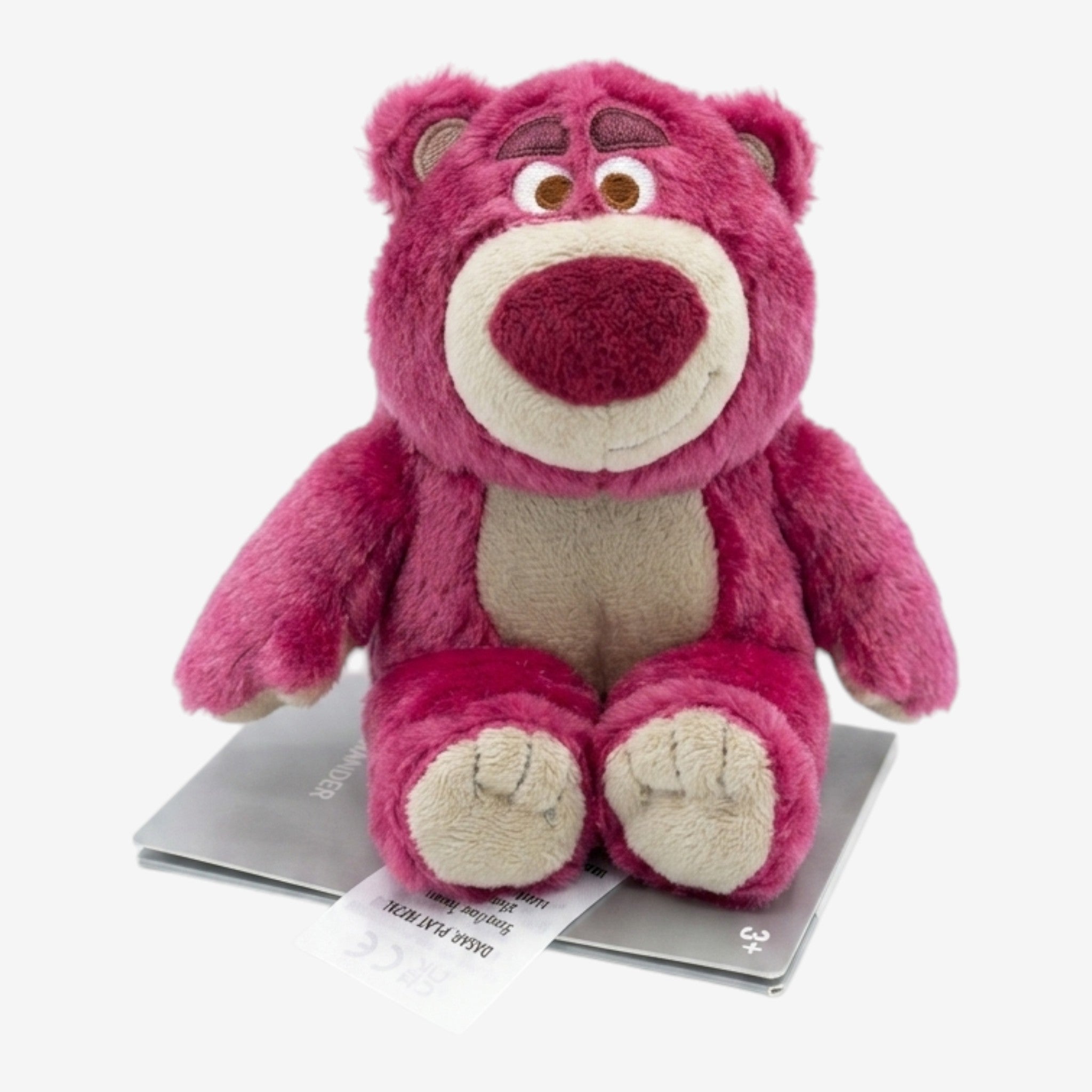 Peluche ours rose Lotso de Once Upon Magic, avec nez rouge et ventre beige, assis sur une carte.